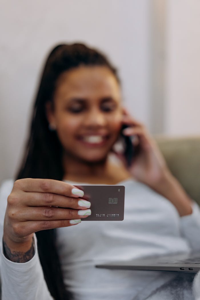 Focused shot of a woman holding a credit card, engaging in a phone conversation, depicting online shopping or banking.